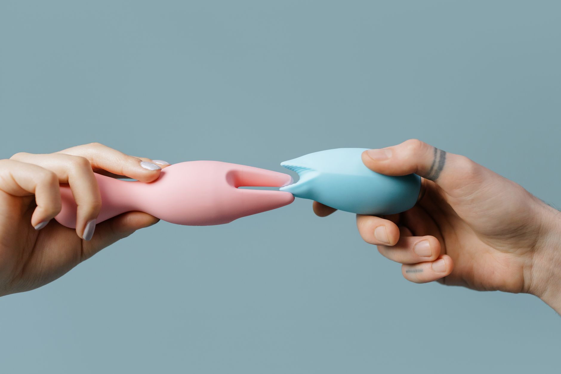Hands holding pastel-colored silicone toys and pleasure devices
