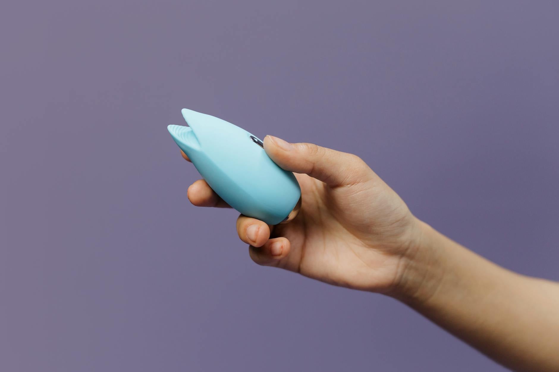 A blue silicone clitoral vibrator held in hand, showcasing its design for external pleasure and couples play.